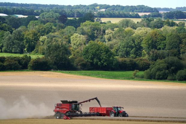 A tractor driving alongside a combine harvester as it unloads grain. Pic: PA.