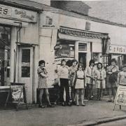 A group of sales assistants and customers outside shops in Gobowen village square